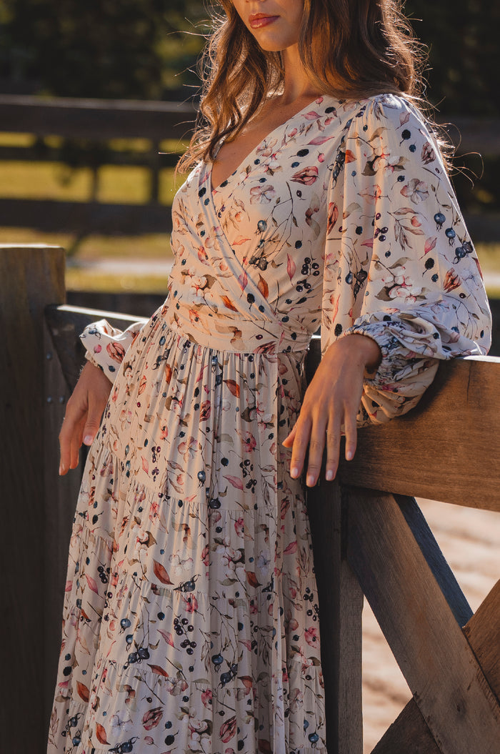 Woman wearing a floral dress leaning against a wooden railing.