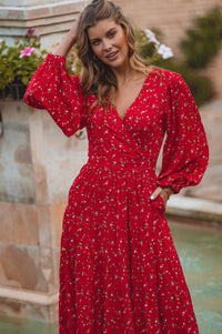 Woman wearing a red dress with floral pattern by a poolside.