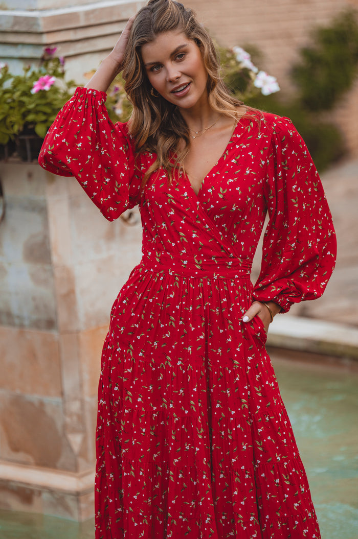 Woman wearing a red dress with floral pattern by a poolside.