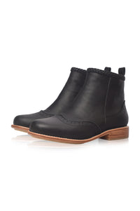 A pair of black leather ankle boots with a low stacked wood-look heel, brogue detailing, and a braided trim at the collar, shown on a white background.