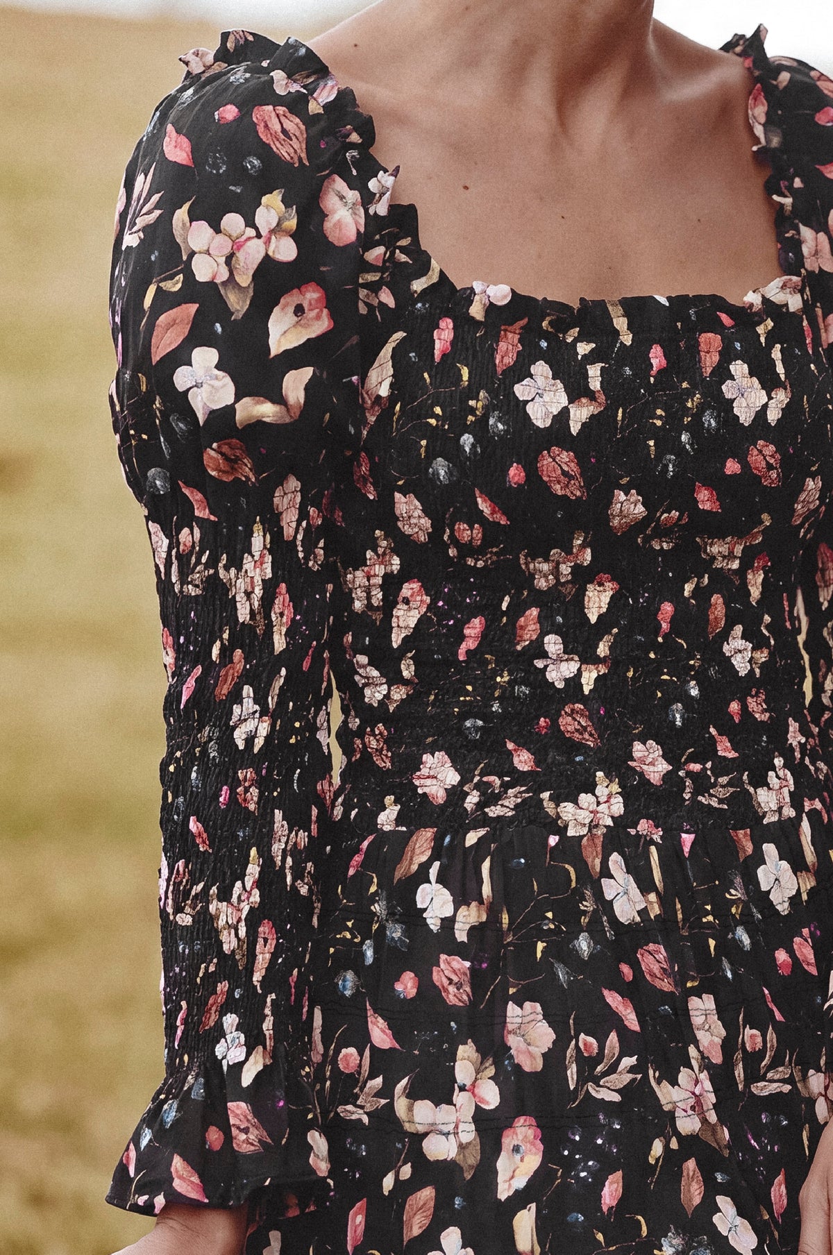 Close-up of a woman wearing a black smocked dress with a pink, white, and beige floral print, featuring puff sleeves and a square neckline.