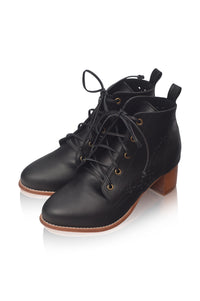 A pair of black leather lace-up ankle boots with low block heels, gold eyelets, and brown soles, shown on a white background with a soft reflection.