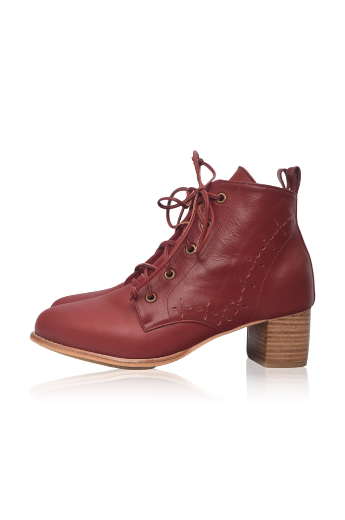 A single red leather lace-up ankle boot with a stacked wood-look block heel, shown in profile against a white background with a soft reflection.