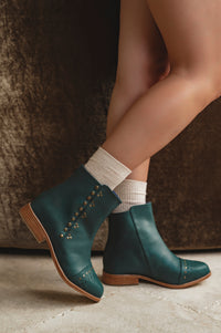 Teal ankle boots with brown soles worn by a person on a neutral background