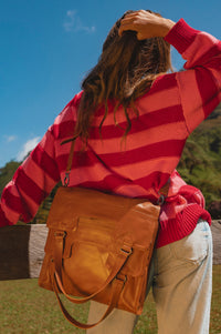 Person wearing a red striped sweater and holding a handmade brown leather bag outdoors.