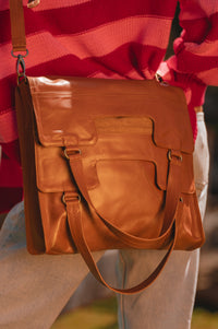 Brown leather bag held by a person wearing a red sweater and light-colored pants.