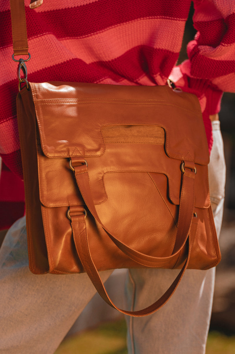 Brown leather bag held by a person wearing a red sweater and light-colored pants.
