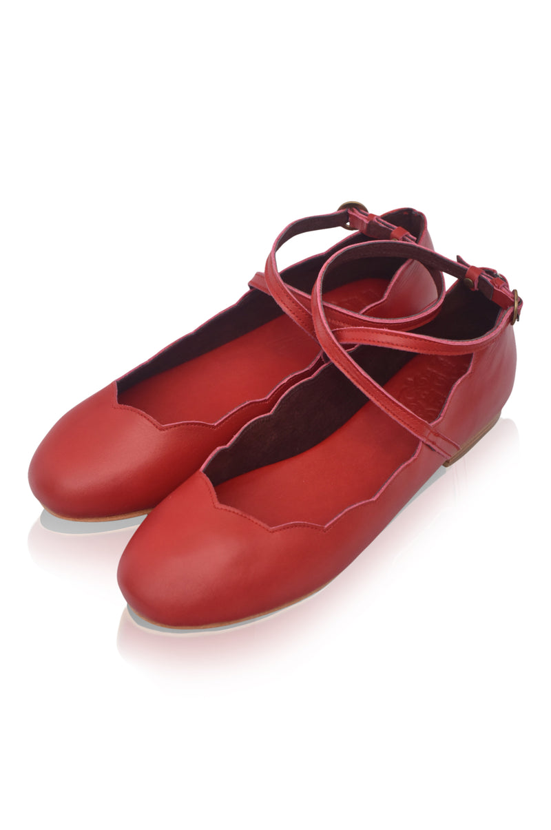 Pair of red ballet flats with a strap on a white background
