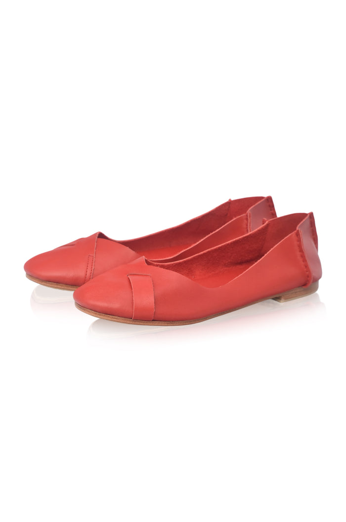 A pair of red leather ballet flats with a pointed toe and a decorative strap detail across the vamp, shown on a white background with a soft reflection.