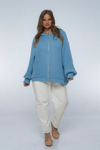 Woman wearing a blue knitted sweater and white pants on a white background