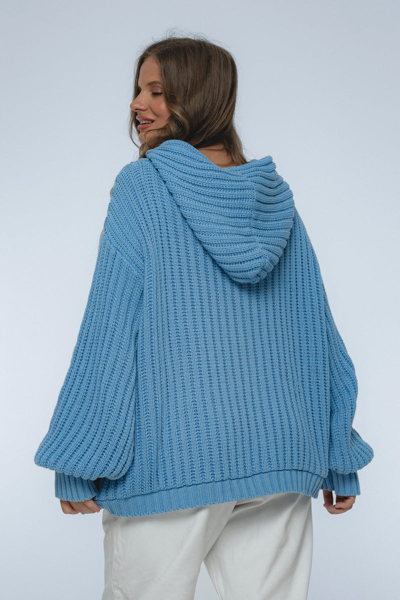 Person wearing a blue knitted hoodie on a plain background