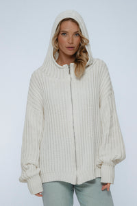 Woman wearing a cream-colored knitted hoodie against a white background