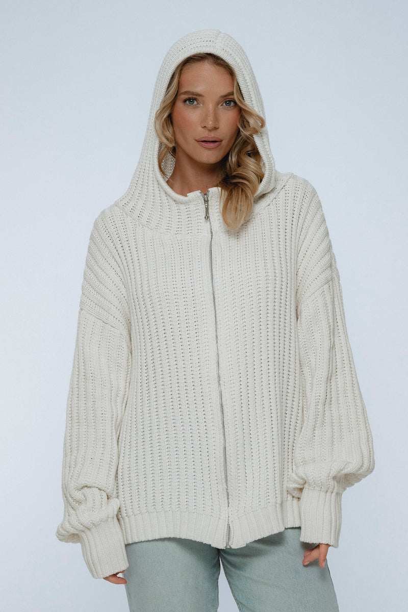 Woman wearing a cream-colored knitted hoodie against a white background
