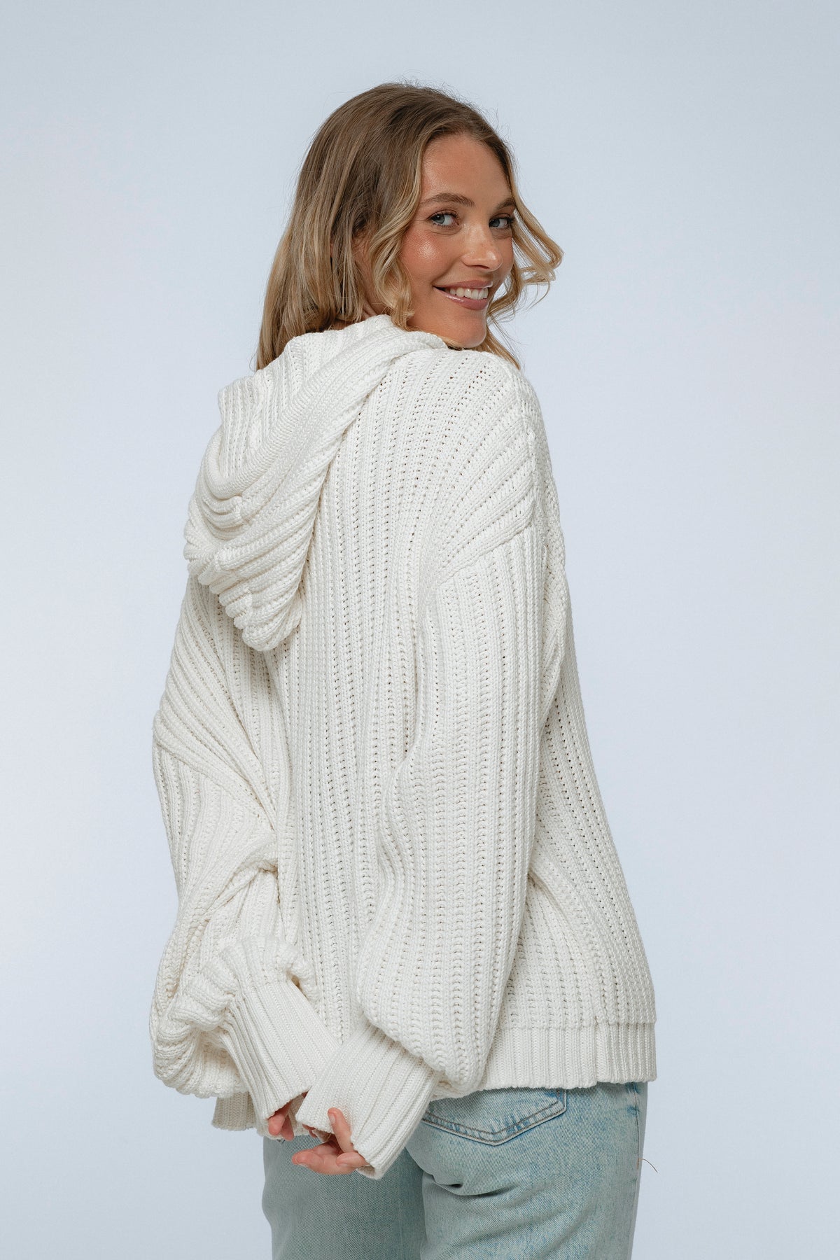 Woman wearing a white chunky knit sweater against a plain background