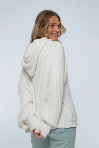 Woman wearing a white chunky knit sweater against a plain background