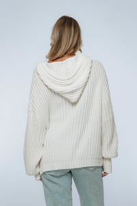 Person wearing a cream-colored knit sweater with a hood on a plain background