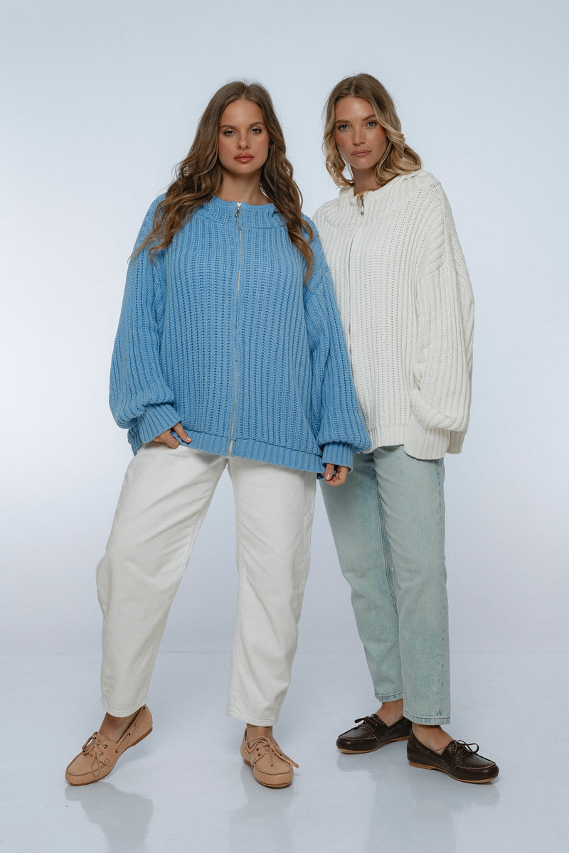 Two women wearing ribbed knit sweaters and pants on a white background