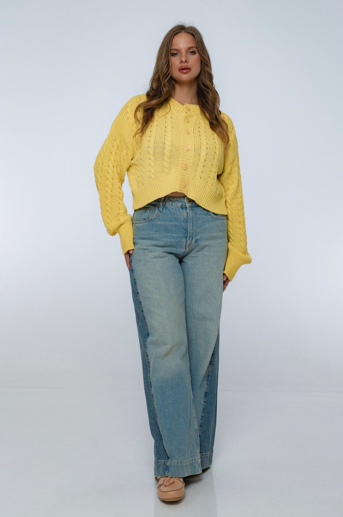 Woman wearing a yellow sweater and blue jeans on a white background