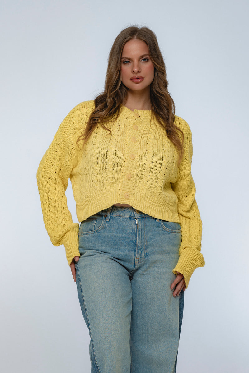 Woman wearing a yellow sweater and blue jeans against a plain background