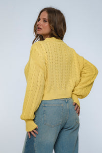 Woman wearing a yellow knitted sweater and blue jeans against a white background