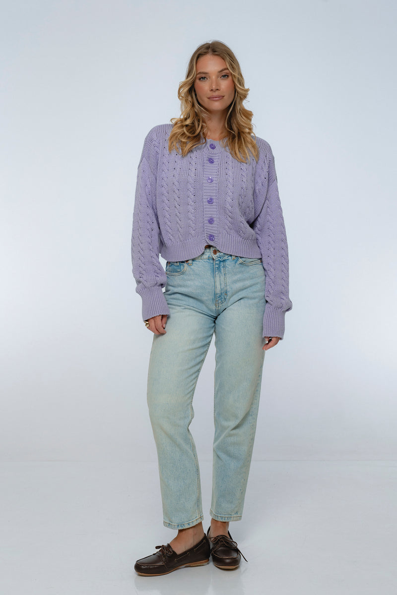 Woman wearing a purple textured sweater and light blue jeans on a white background