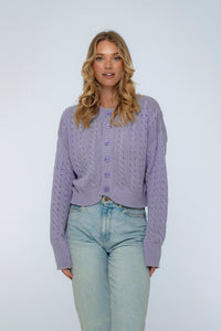 Woman wearing a light purple knitted cardigan and light blue jeans on a white background