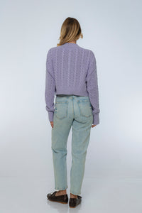 Person wearing a purple sweater and light blue jeans on a white background