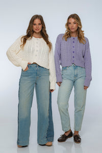 Two women wearing knitted cardigans and jeans on a white background