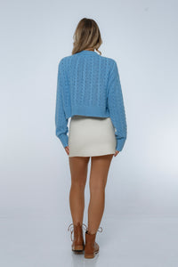 Person wearing a blue knitted sweater and beige skirt on a white background