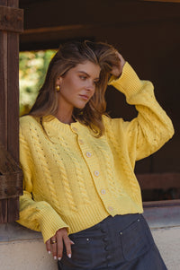 Woman wearing a yellow knitted cardigan standing outdoors.