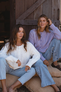 Two women sitting on a rustic wooden staircase wearing light-colored clothing.