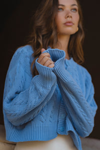 Woman wearing a blue knitted sweater against a dark background