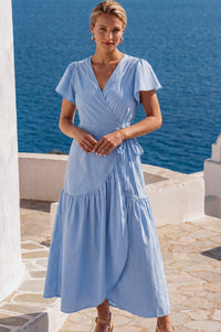 Woman in a light blue dress standing by a scenic waterfront.