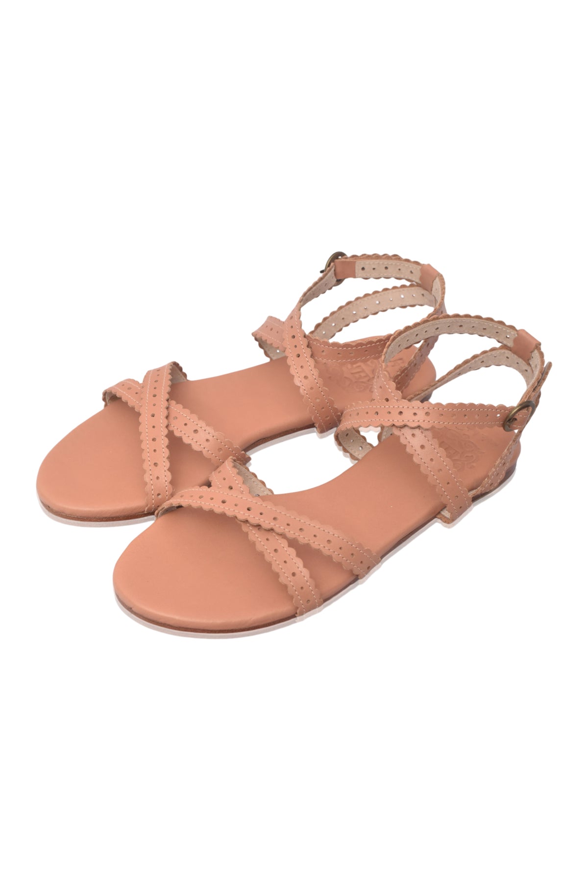 A pair of women's flat sandals in a light peach-beige color, featuring criss-crossing perforated straps and adjustable ankle straps, shown on a plain white background.
