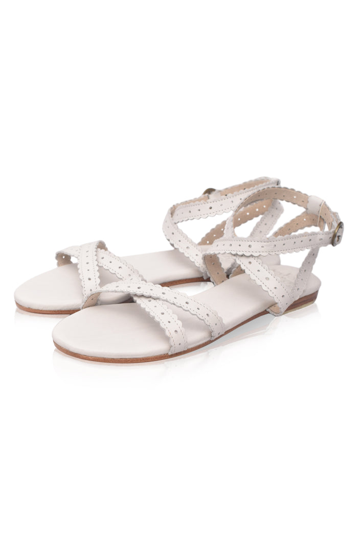 A pair of women's flat sandals in a light cream or off-white color, featuring perforated straps and an adjustable ankle strap, shown on a plain white background.