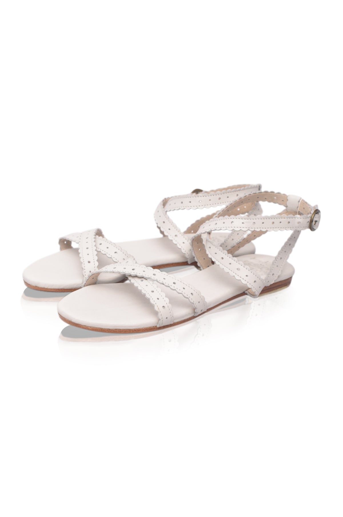 A pair of women's flat sandals in a light cream or off-white color, featuring perforated straps and an adjustable ankle strap with a small silver buckle, shown on a plain white background.
