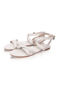A pair of women's flat sandals in a light cream or off-white color, featuring perforated straps and an adjustable ankle strap with a small silver buckle, shown on a plain white background.