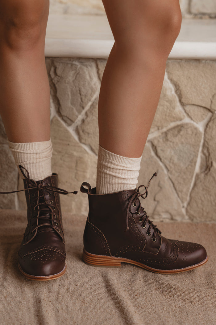 Brown lace-up boots worn with white socks against a stone wall background