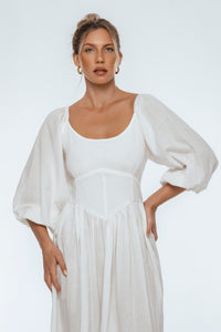 Woman wearing a white dress with puffed sleeves against a plain background