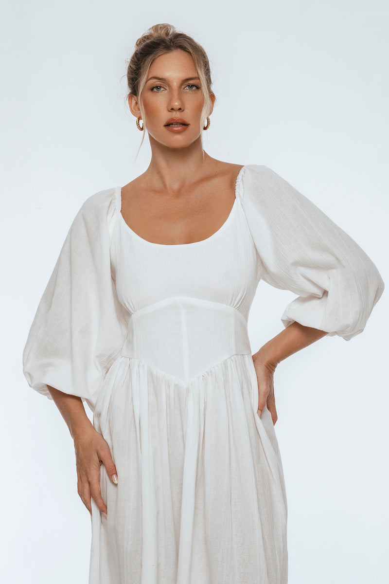 Woman wearing a white dress with puffed sleeves against a plain background