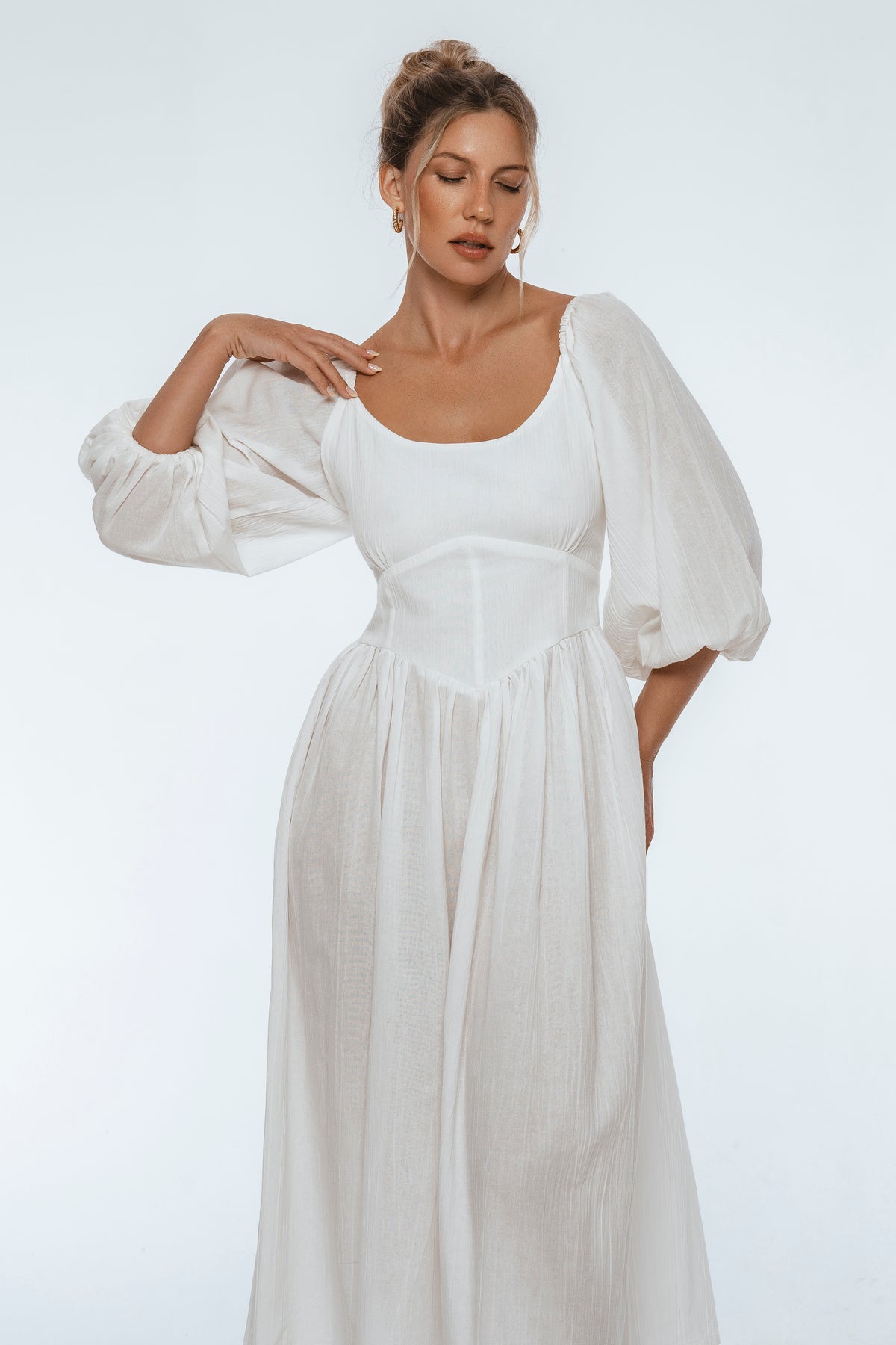 Woman wearing a white dress with puffed sleeves on a plain background