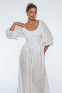 Woman wearing a white dress with puffed sleeves on a plain background