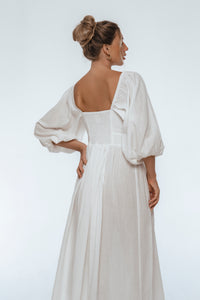 Woman wearing a white dress with puffed sleeves on a plain background