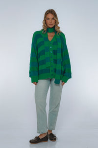 Woman wearing a green and blue striped sweater with light gray pants on a white background