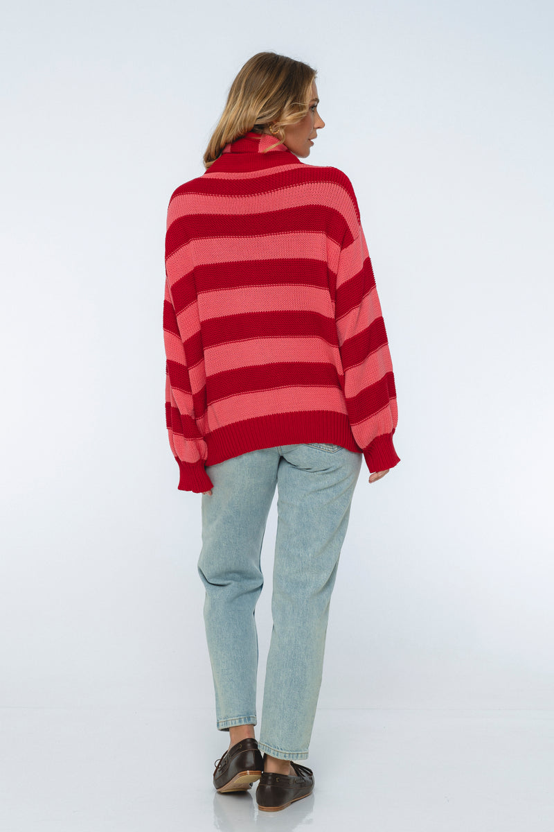 Person wearing a red and pink striped sweater with light blue jeans on a white background