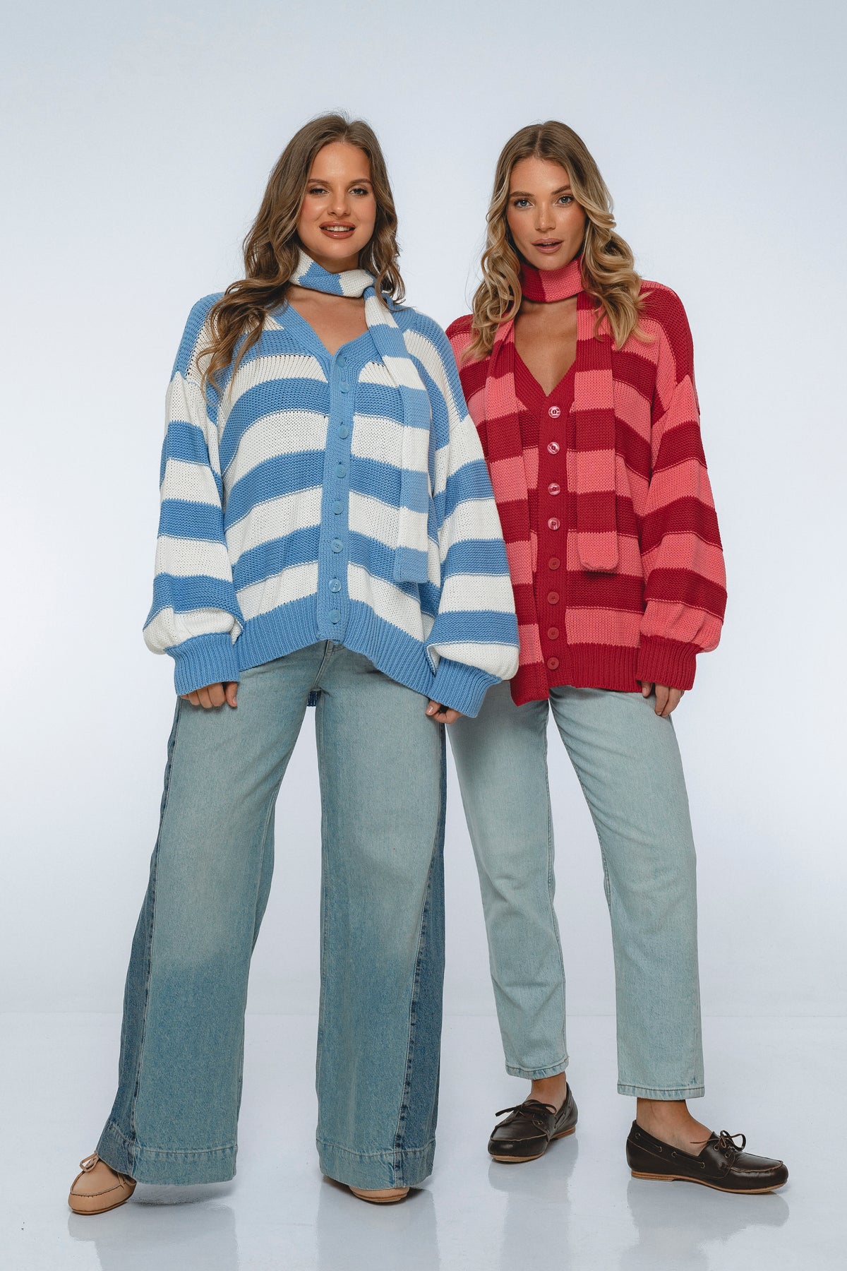 Two women wearing colorful cardigans and jeans on a white background