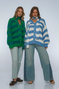 Two women wearing colorful striped sweaters and jeans on a white background