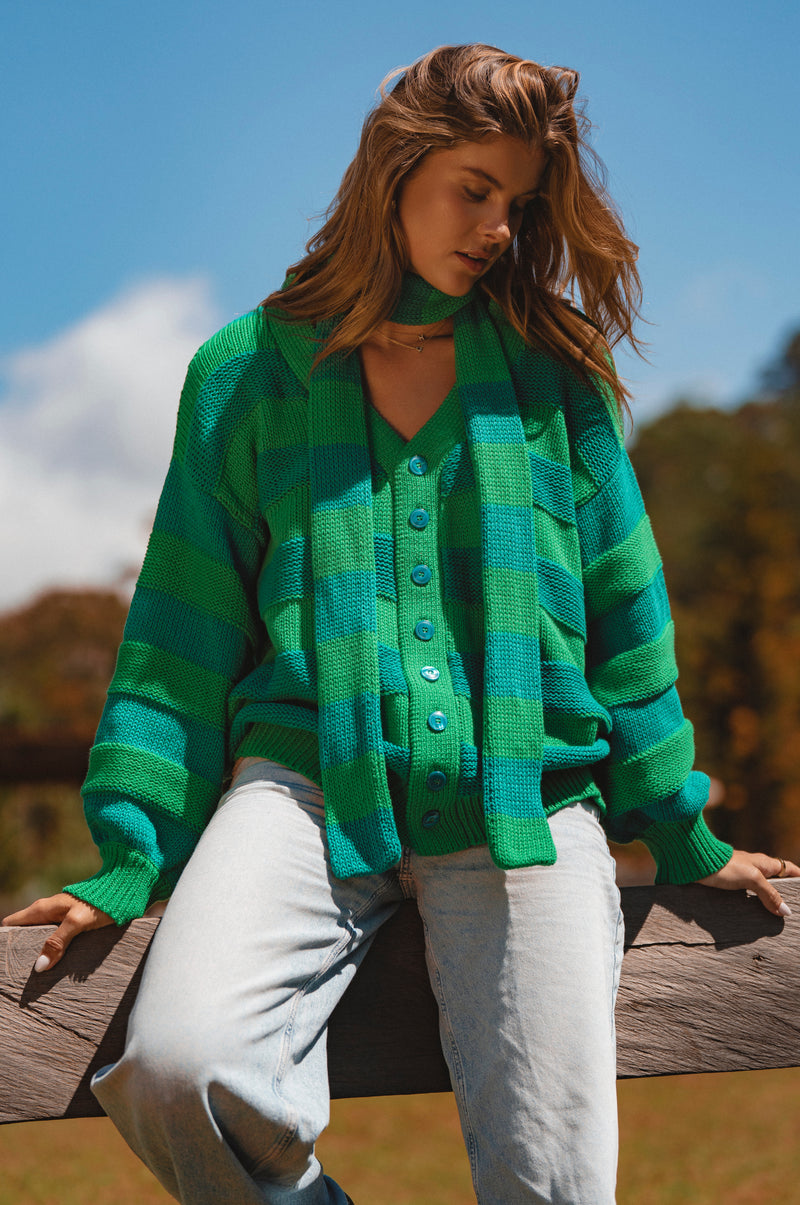 Woman wearing a green plaid cardigan outdoors with a blurred natural background
