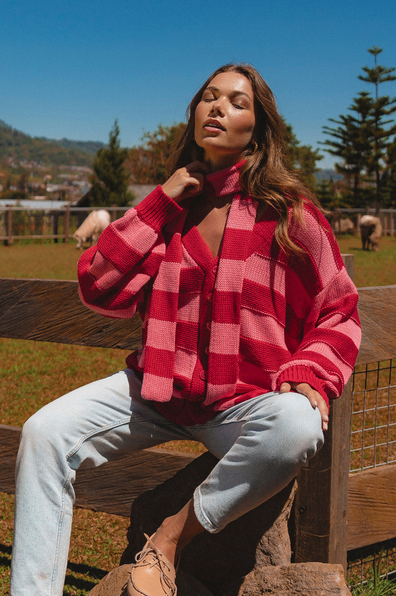 Woman wearing a red and pink checkered sweater sitting on a wooden bench outdoors.