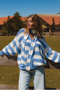 Woman wearing a blue and white striped sweater in an outdoor setting with trees and a building in the background.